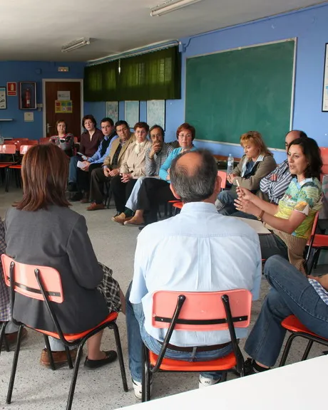 Grup de mares i pares reunits a una aula escolar.