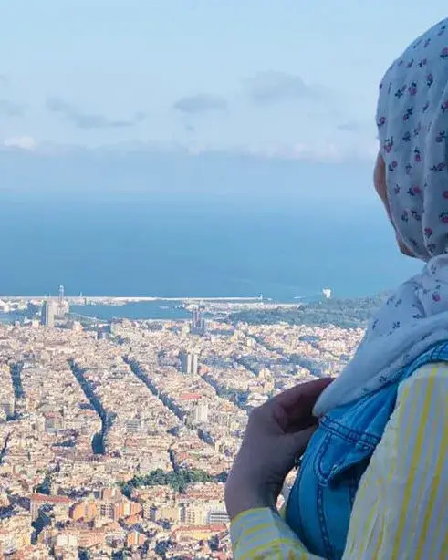 Una noia que porta hijab mira, d'esquena a càmera, les vistes de la ciutat de Barcelona