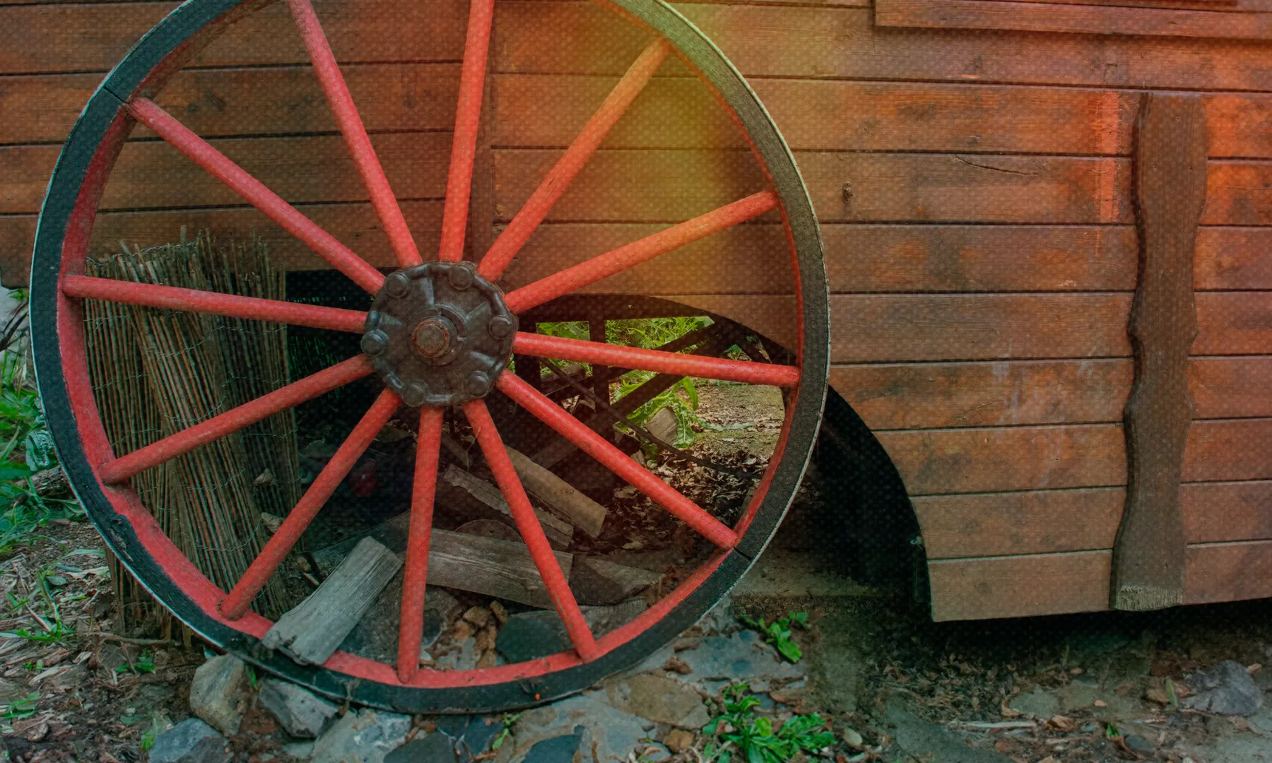 Roda d’un carro de fusta tradicional amb radis vermells davant d’una caravana de fusta.