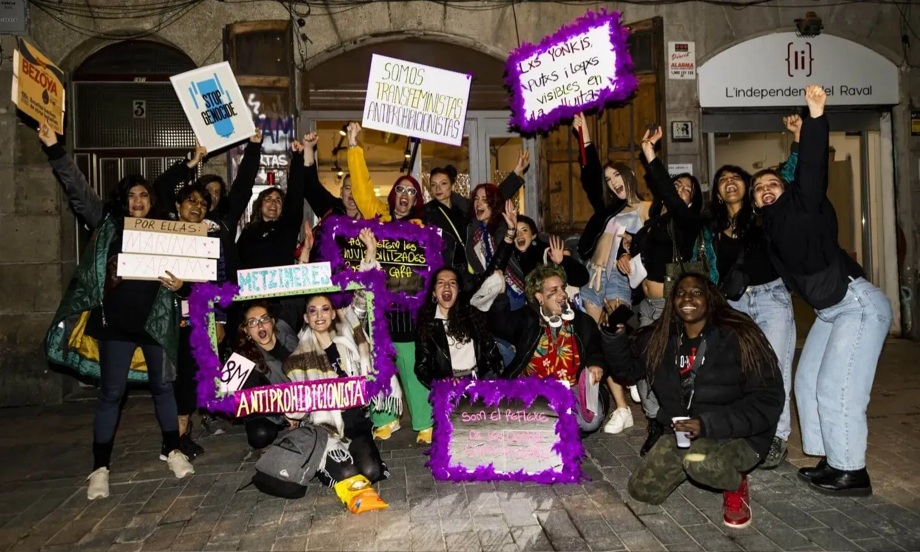 Grup de dones i persones de gènere divers en una acció al carrer, sostenint pancartes amb missatges feministes i antiprohibicionistes davant un local al barri del Raval.