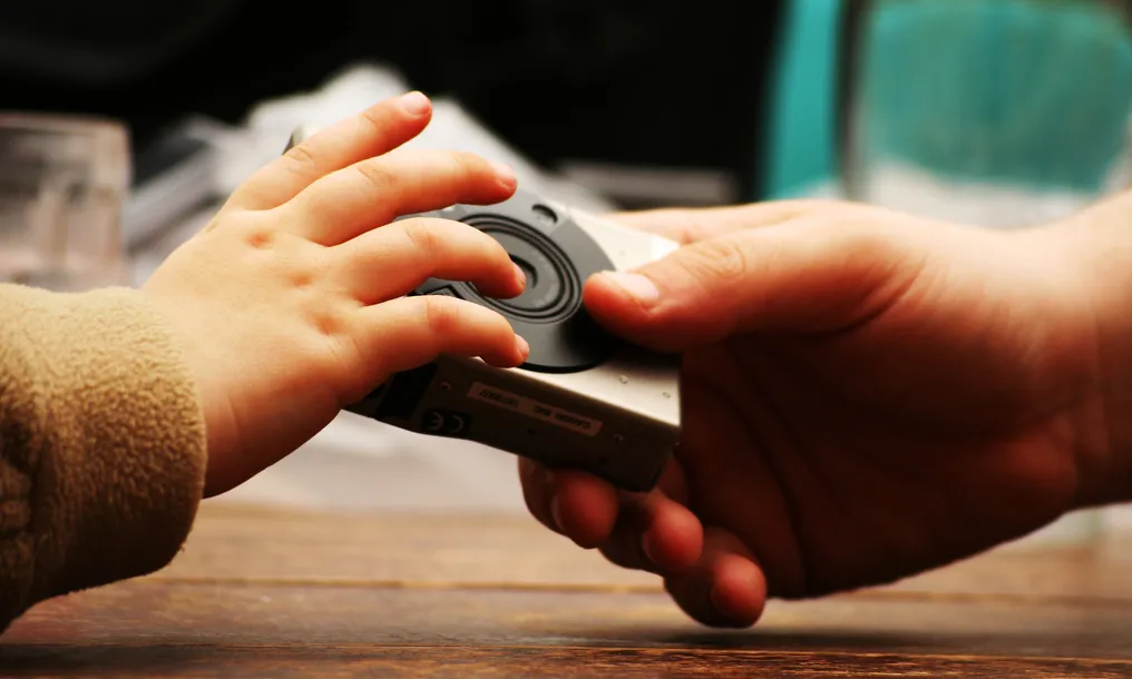 Una mà adulta li dóna una càmera de fotos a una mà infantil