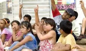 Infants asseguts al terra amb les mans aixecades. Font: web estris.cat
