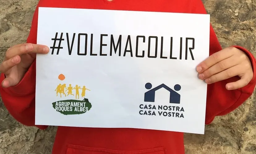 Les mans d'un infant sostenint un cartell fet per l'Agrupament Roques Albes per a donar suport a la manifestació