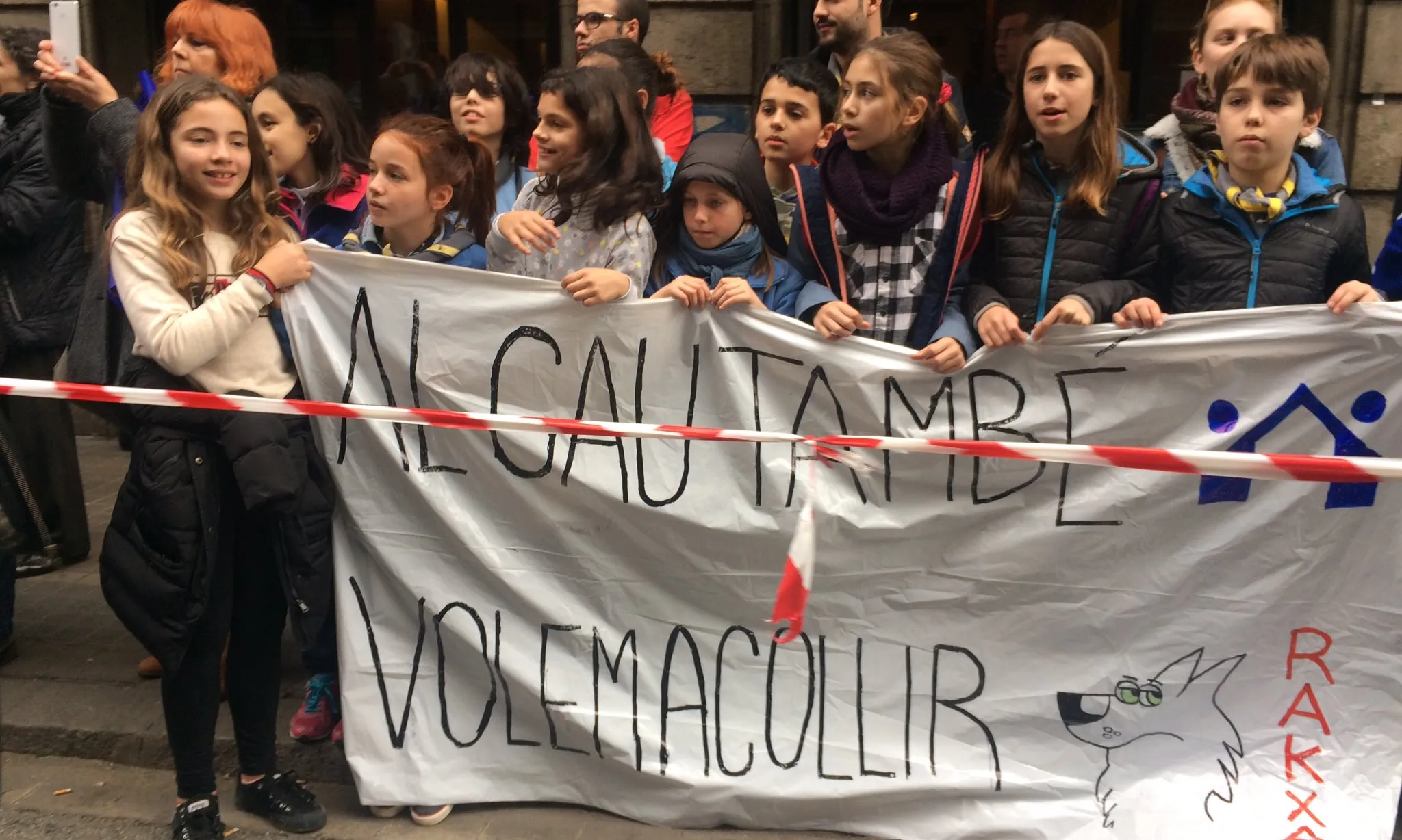 Un grup d'infants escoltes a la manifestació #VolemAcollir amb una pancarta que diu "Al cau també volem acollir"