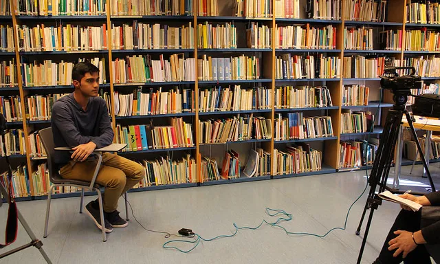 Un jove explicant les seves reflexions davant de la càmara, en una biblioteca.