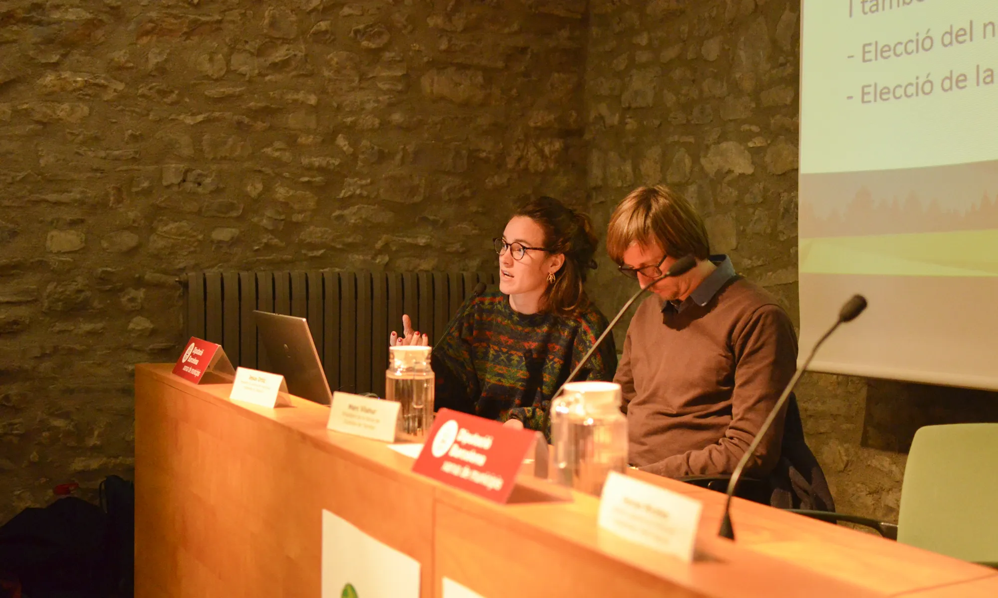 La Mireia Salazar, jurista de la XCT, explica el procediment a seguir durant l'assemblea. Està asseguda al costat d'en Marc Vilahur, president de la XCT, i utilitza el micro per explicar el projecte de fusió als socis de la XCT-XVAC.