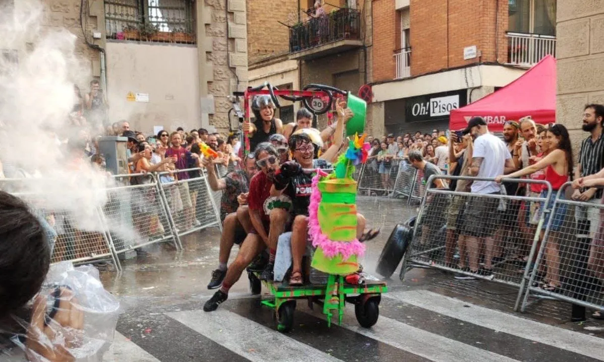 Un grup de persones sobre un carretó envoltats de gent que els anima i els llença aigua.