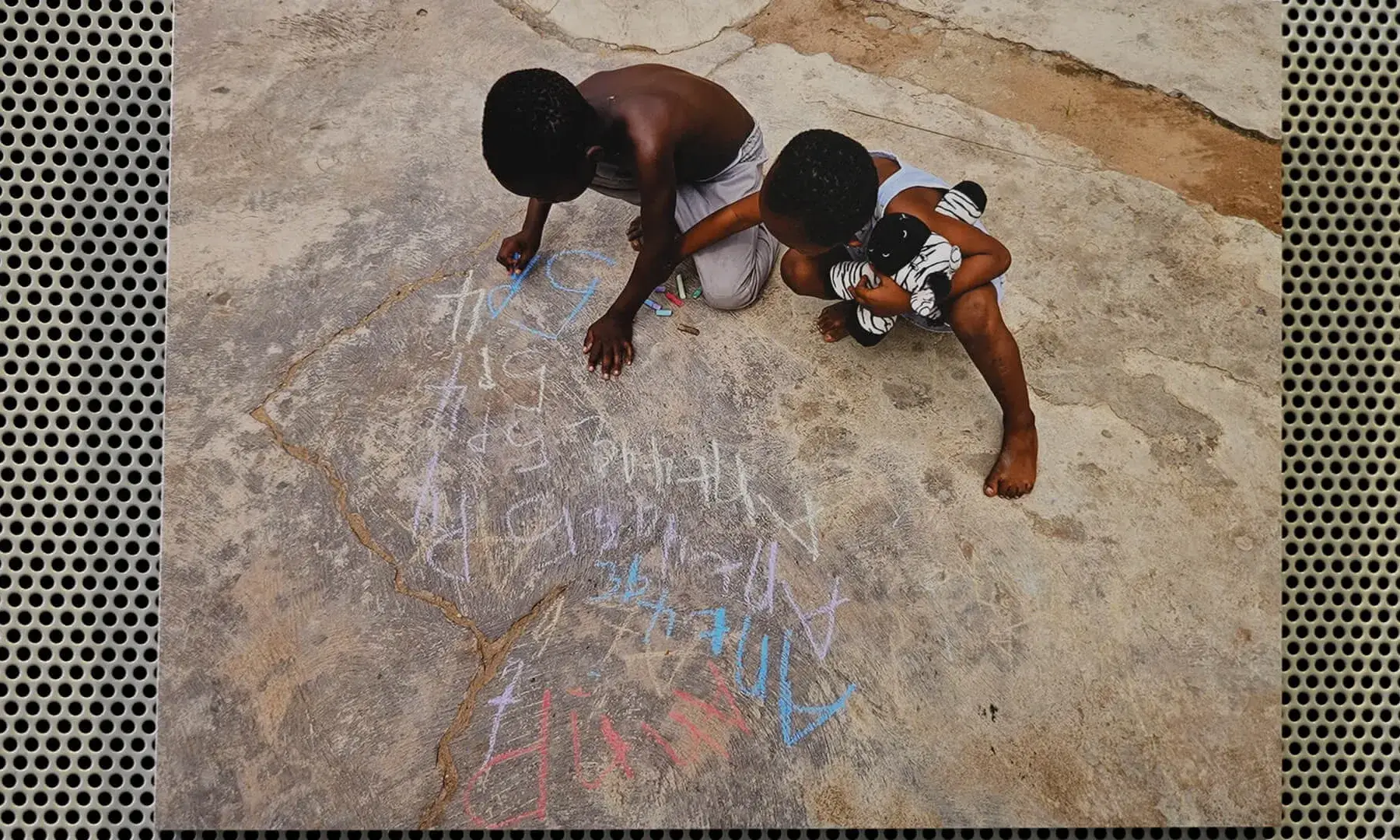 Una imatge de dos infants africans dibuixant amb guixos de colors el terra.