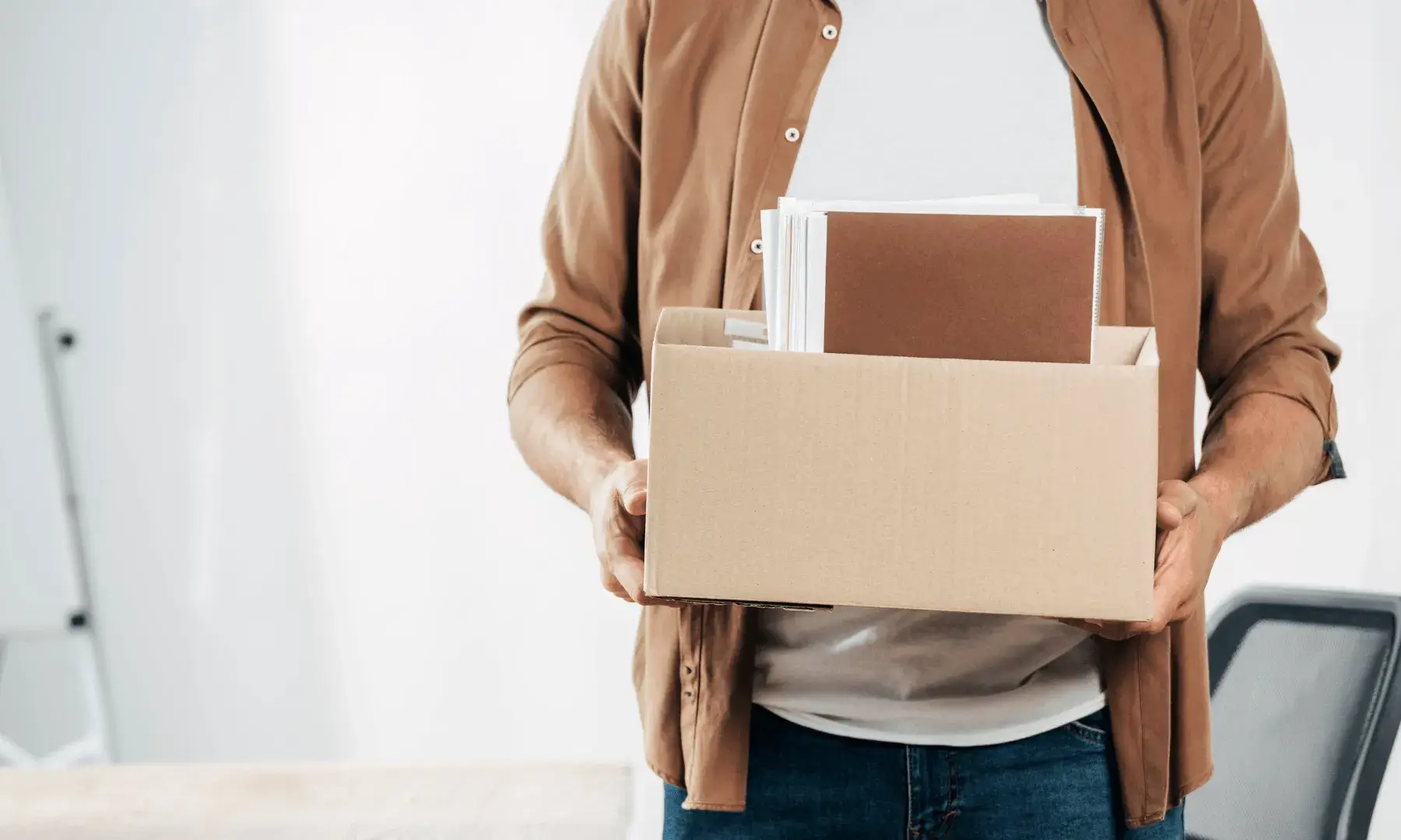Persona sostenint una caixa amb objectes personals en un entorn de treball, simbolitzant un acomiadament laboral.