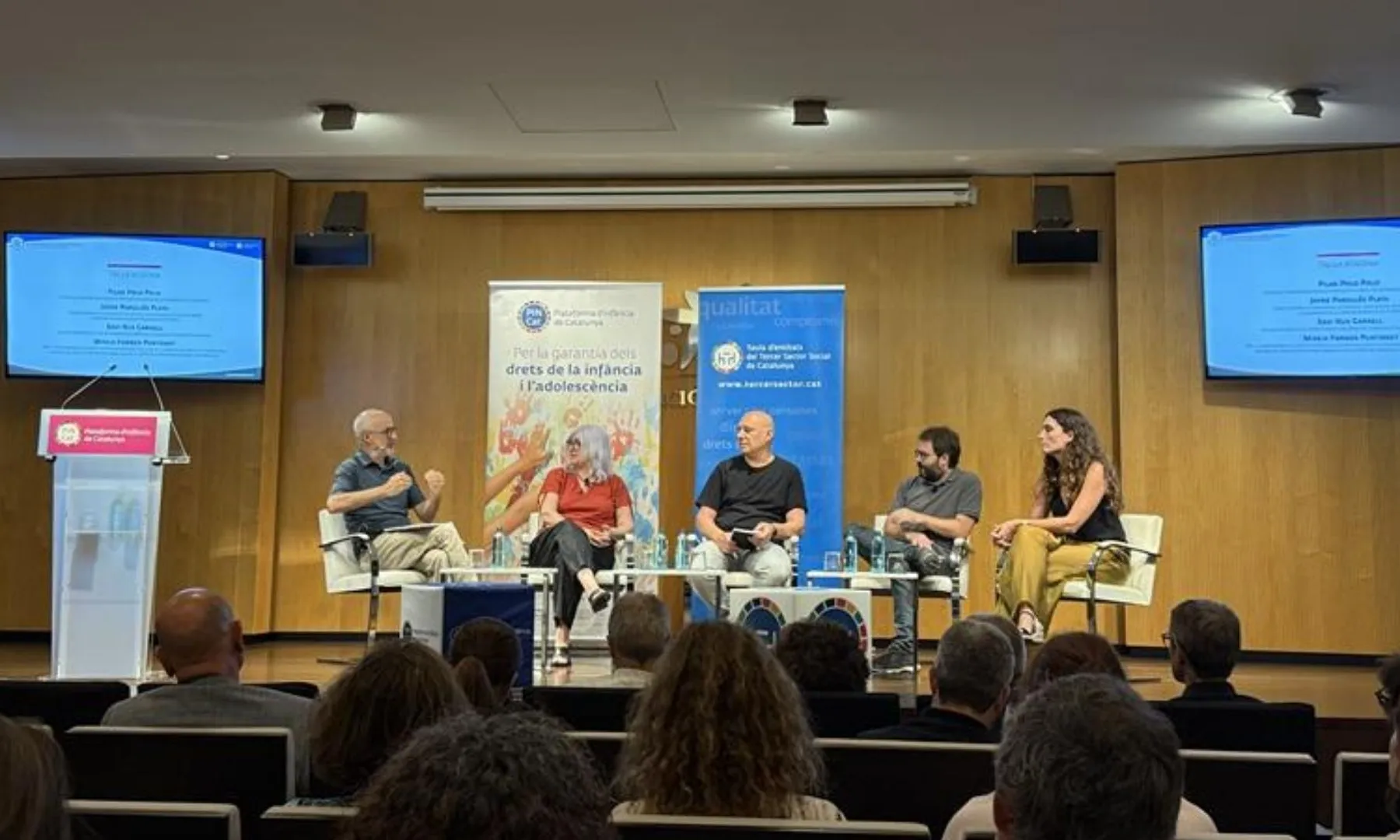 Quatre persones participen en una taula rodona sobre la protecció dels drets de la infància i l'adolescència davant del públic.