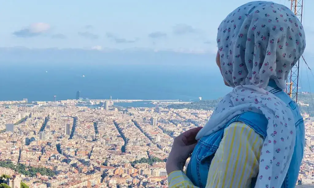 Una noia que porta hijab mira, d'esquena a càmera, les vistes de la ciutat de Barcelona