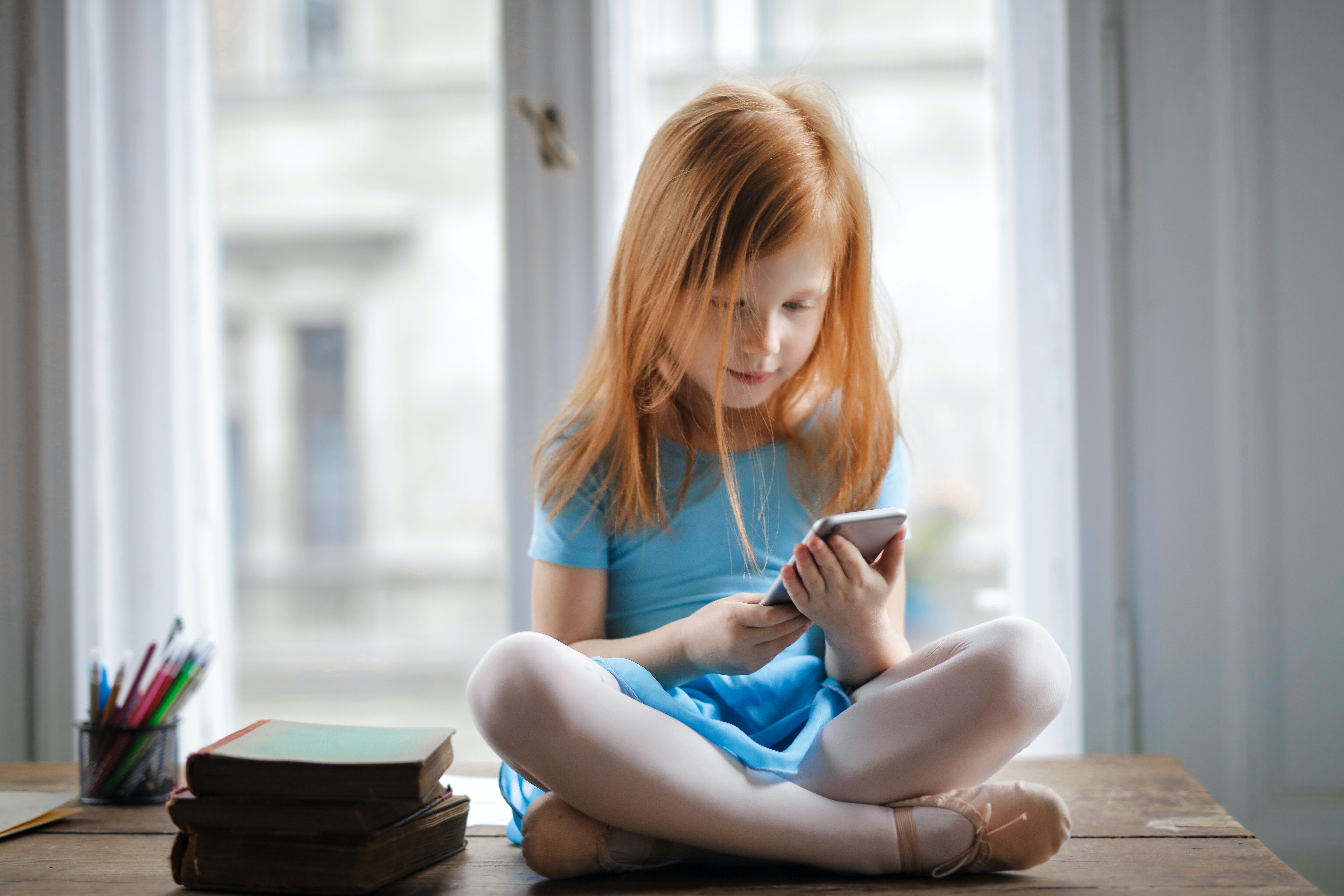 Una nena es mira un telèfon mòbil. Font: Andrea Piacquadio (Pexels)
