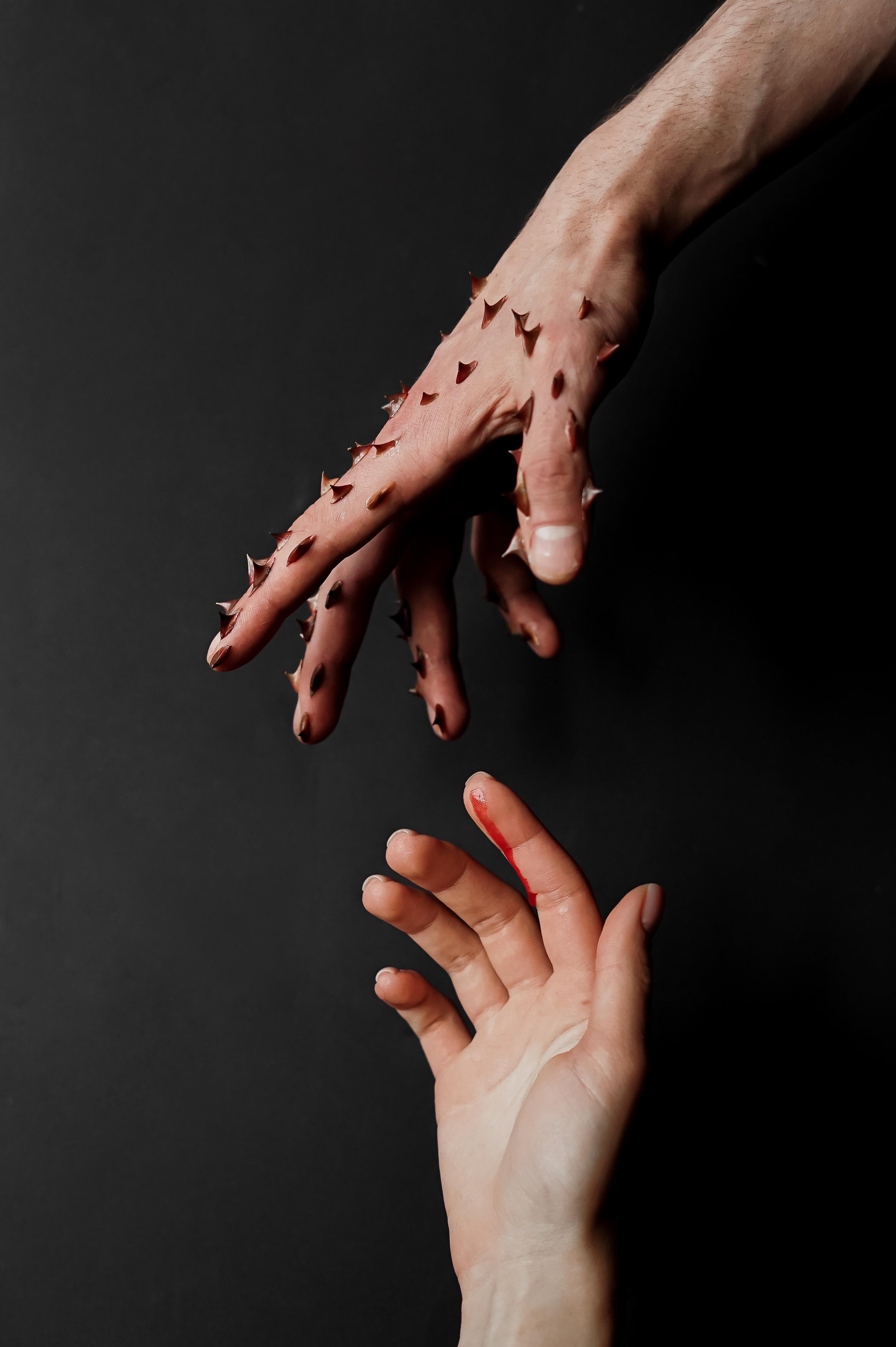 Mà plena de punxes que va a agafar un altre mà. Font: Pexels - Anna Shevchuk