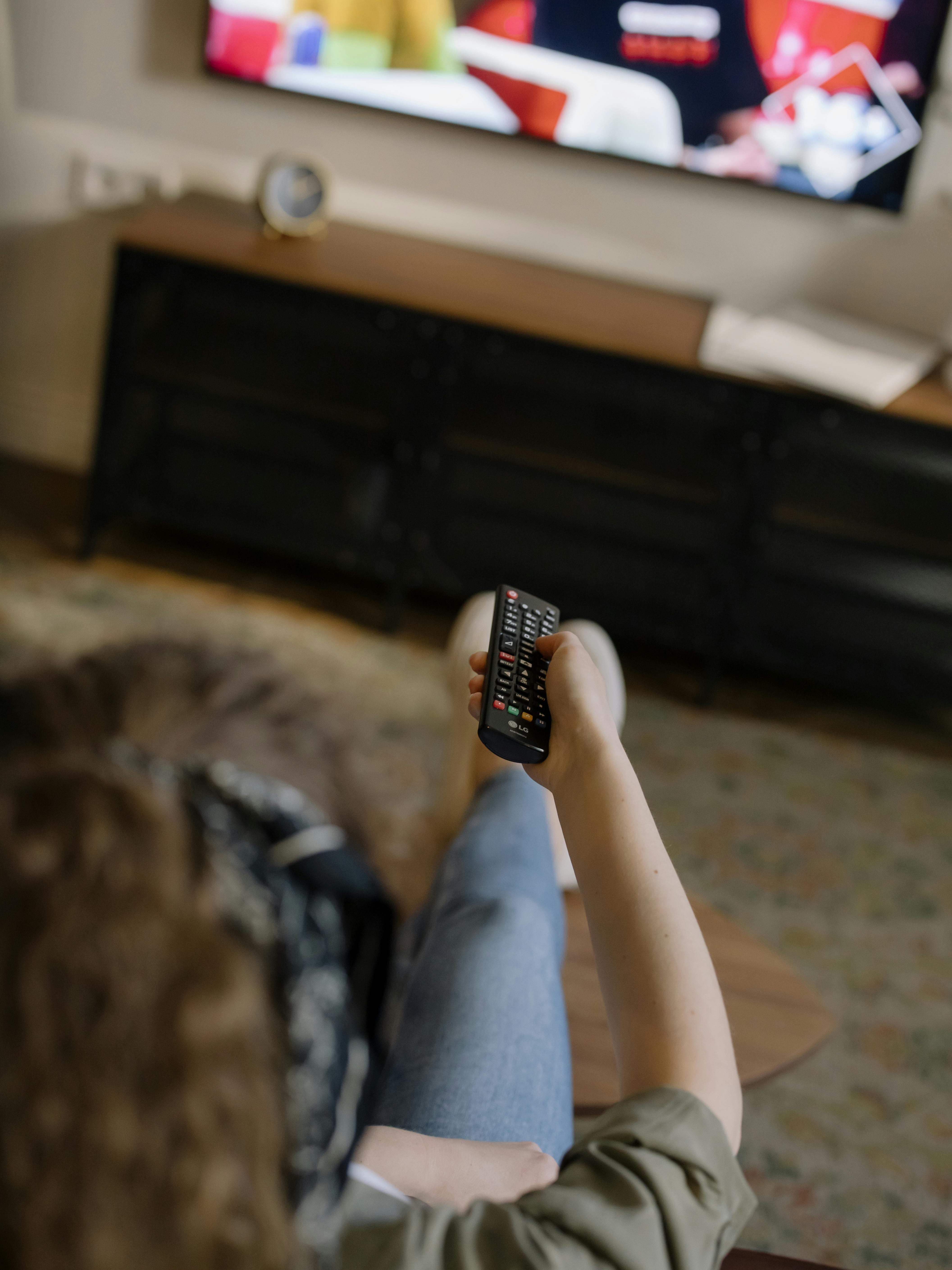 Persona amb un comandament a distància enfocant a una televisió. Font: Pexels - cottonbro studio