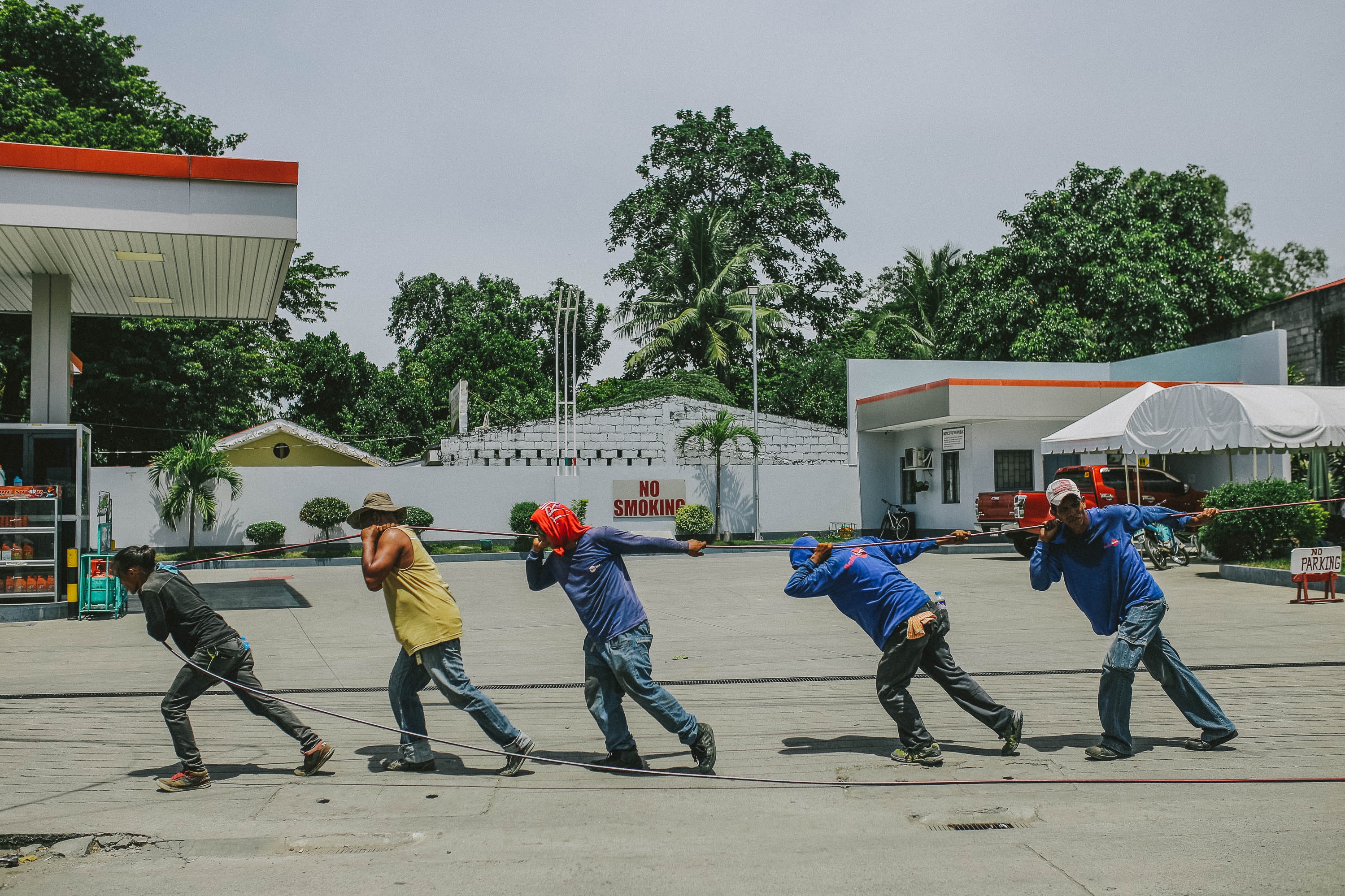 Treballadors en una benzinera, estirant una corda. Font: Pexels - Denniz Futalan