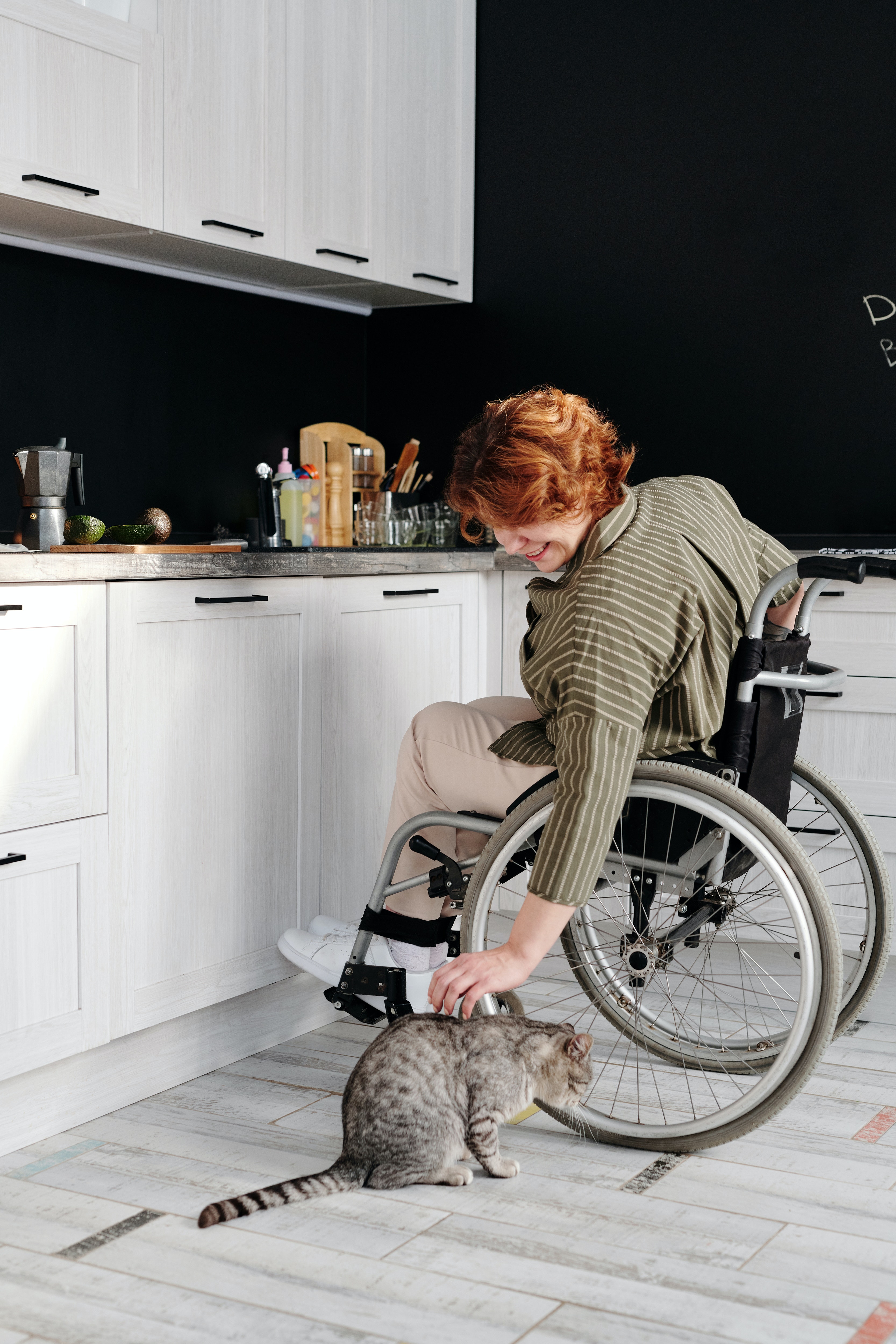 Persona en cadira de rodes a la cuina acariciant un gat. Font: Pexels - Marcus Aurelius