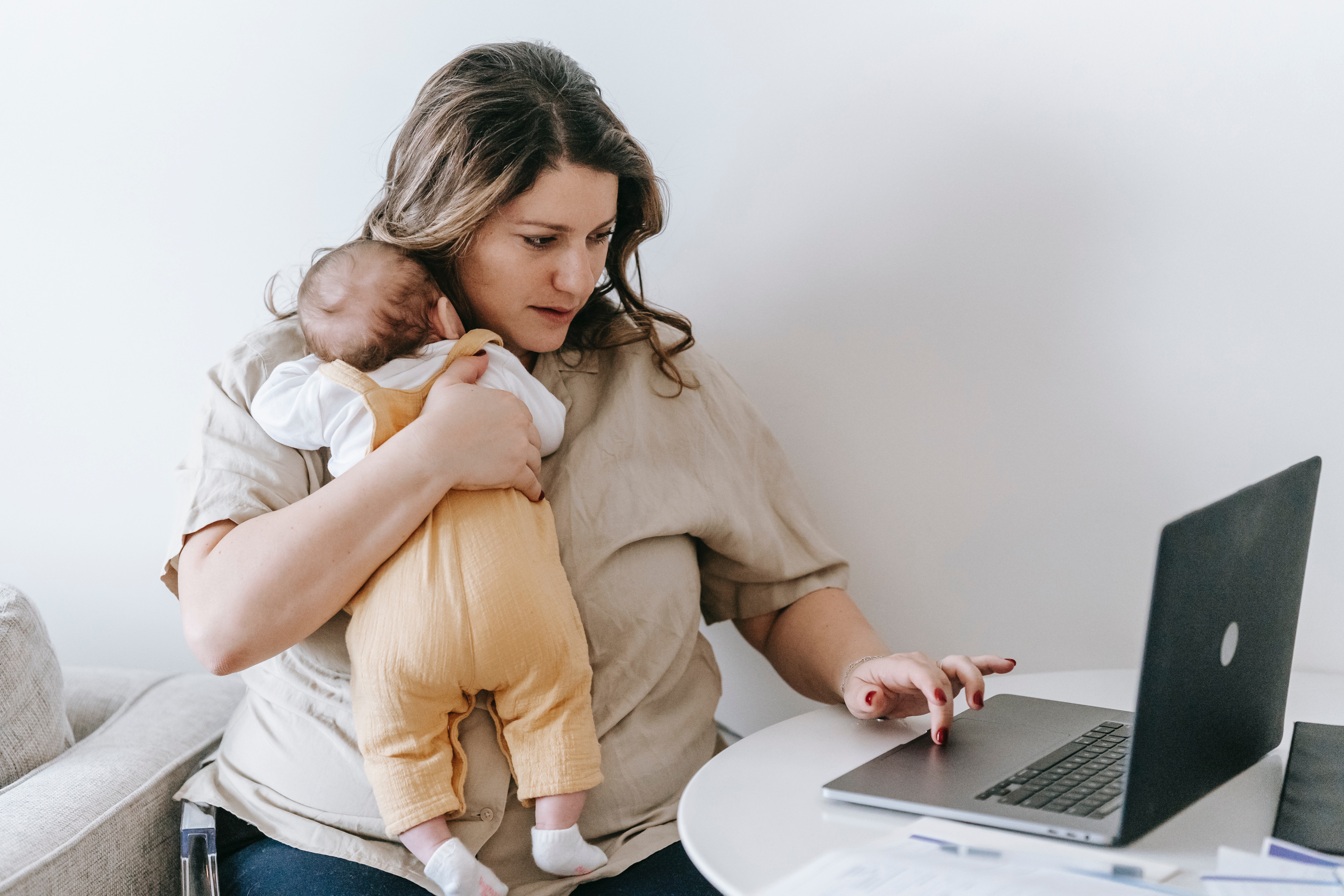 Dona amb un nadó en braços i escrivint a l'ordinador. Font: Pexels - Sarah Chai
