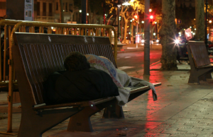 Persona sense llar dorm al carrer enmig de la nit.  Font: Voluntaris.cat