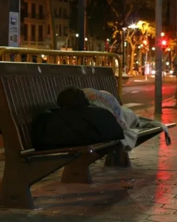 Persona dormint estirada a un banc del carrer de la ciutat de Barcelona.  Foto: Arrels Fundació