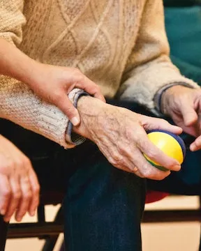 Cuidadora agafant la mà d'una persona gran que té una pilota. Font: Matthias Zomer