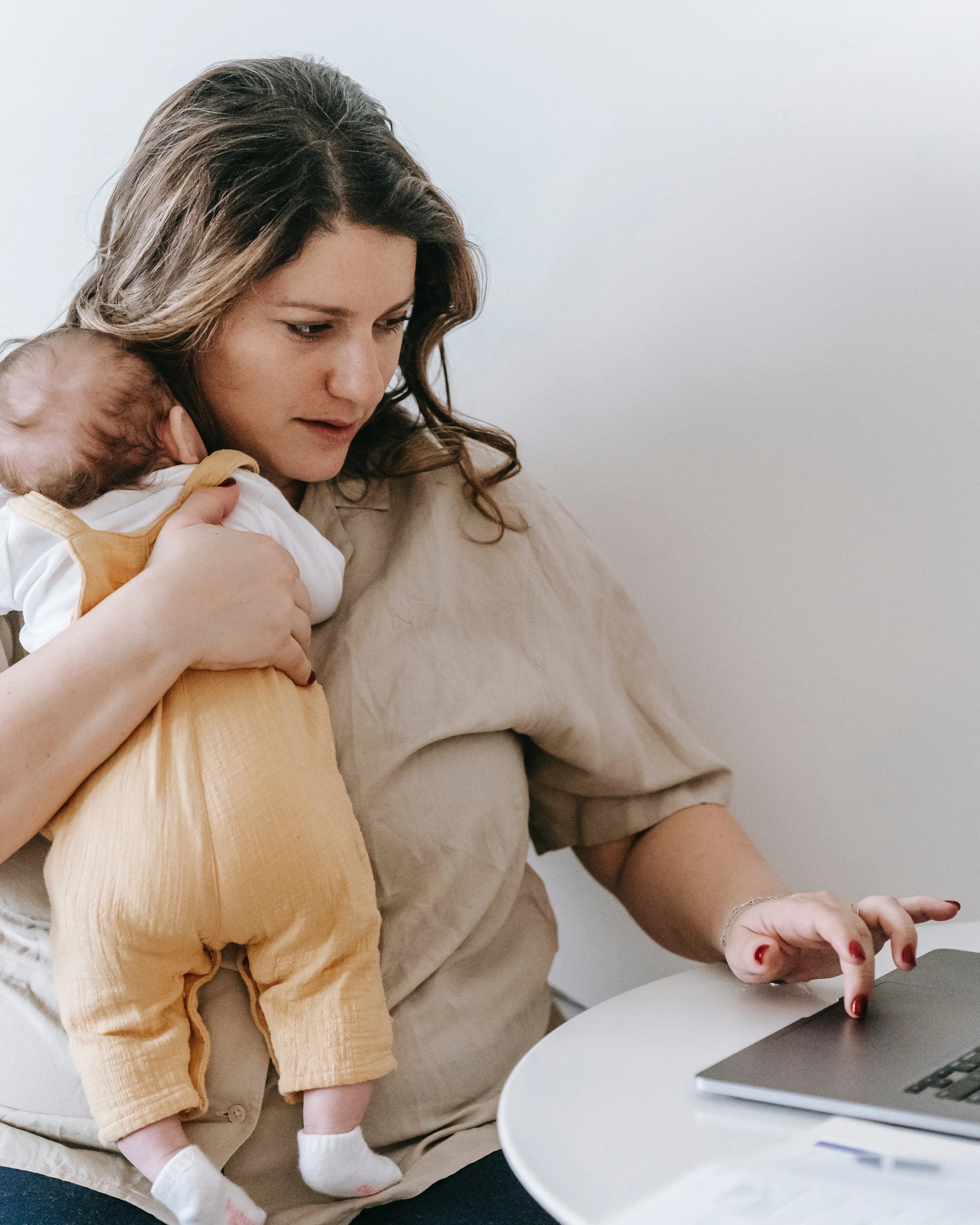 Dona amb un nadó en braços i escrivint a l'ordinador. Font: Pexels - Sarah Chai