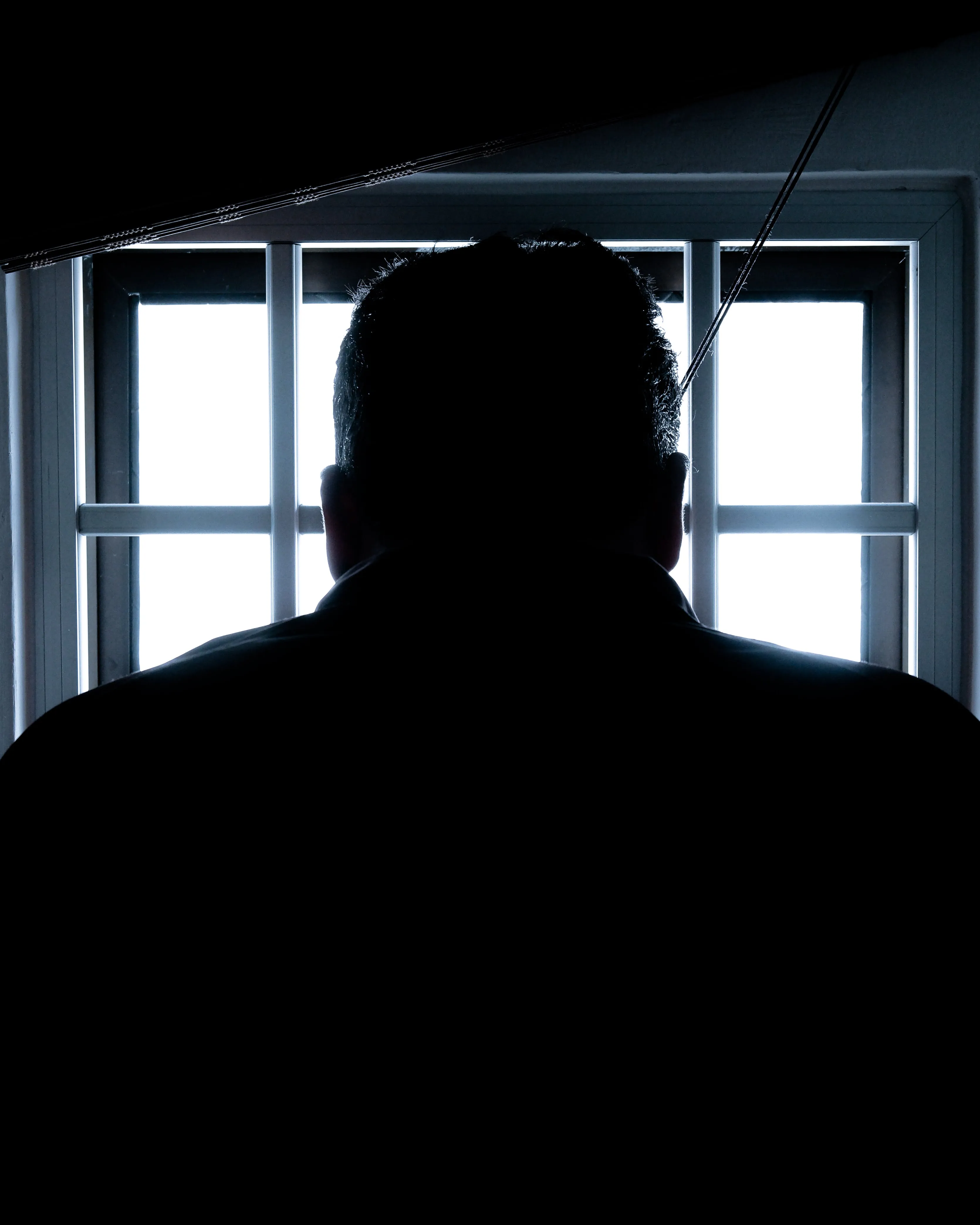 Persona mirant per una finestra amb reixa. Font: Pexels - Donald Tong