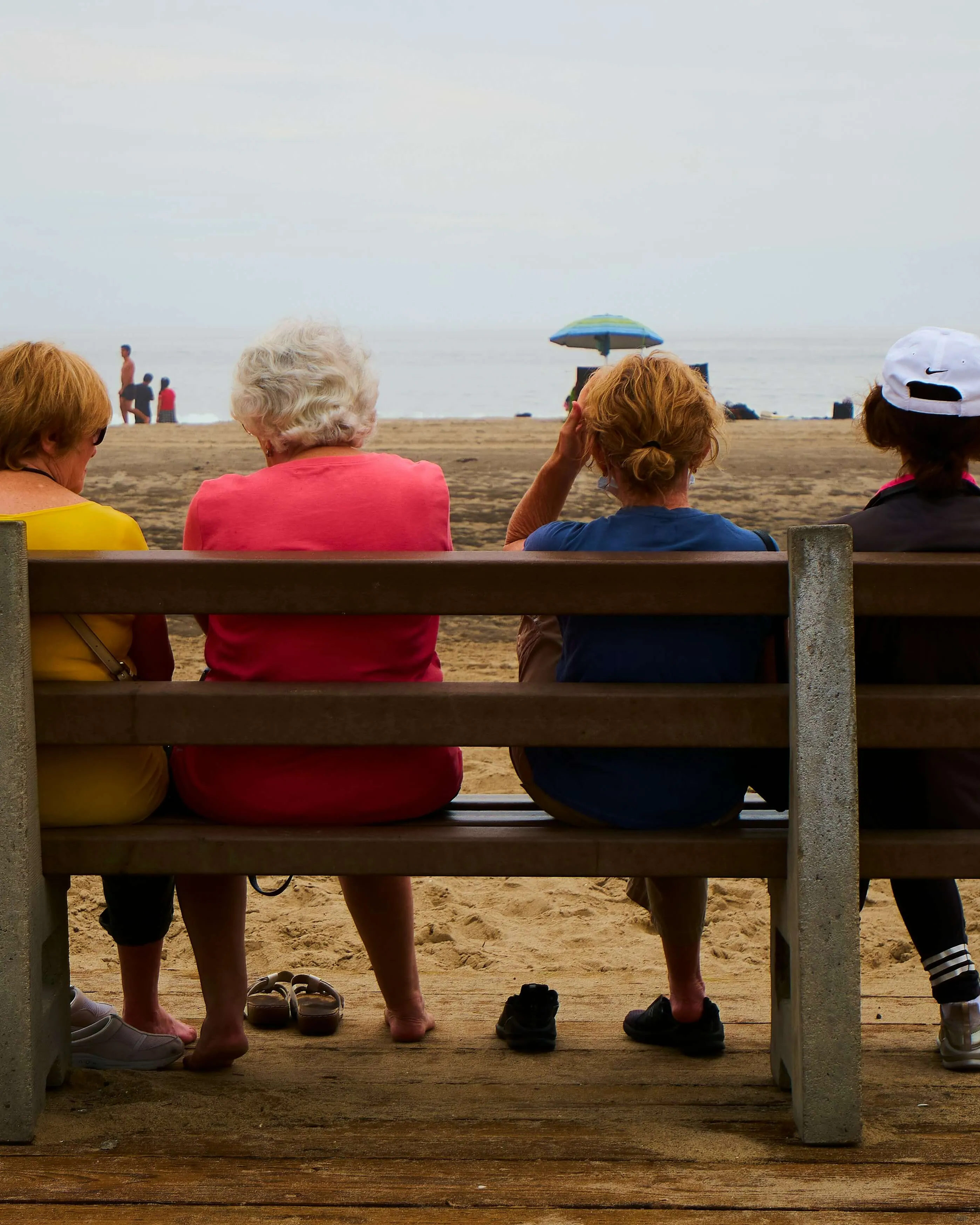 Gent gran asseguda en companyia en un banc davant de la platja.