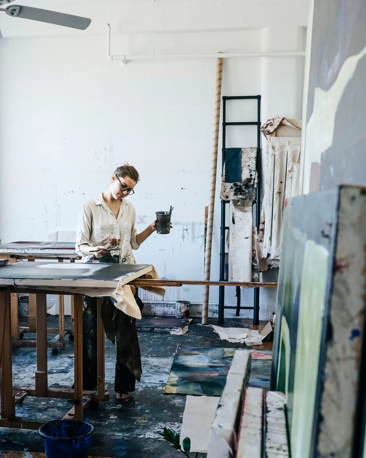 Una artista treballa en un gran llenç en un estudi, envoltada de material artístic.