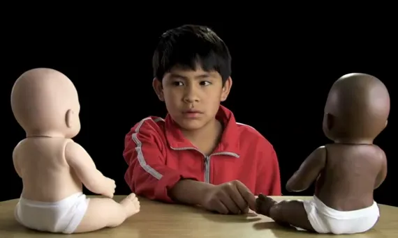 Fotograma amb un nen davant 2 ninots del vídeo de la campanya Racismo en México