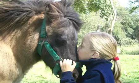 Nena fent un petó a un cavall. Equinoteràpia.