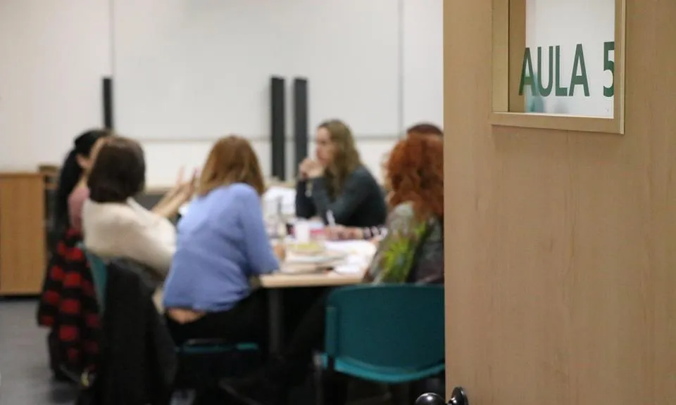 Porta obert a un aula amb dones reunides al voltant d'una taula