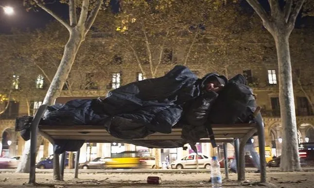 Una persona sense sostre dorm en un banc al costat de la Ciutadella