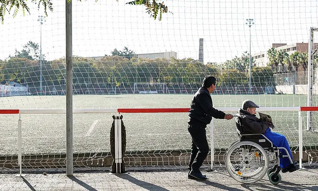 Una persona acompanya a una altra amb cadira de rodes 