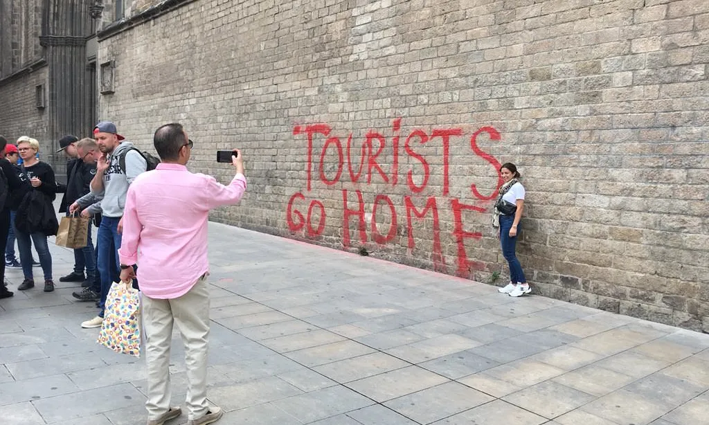 Turistes fent-se fotos davant d'una pintada de denúncia del turisme