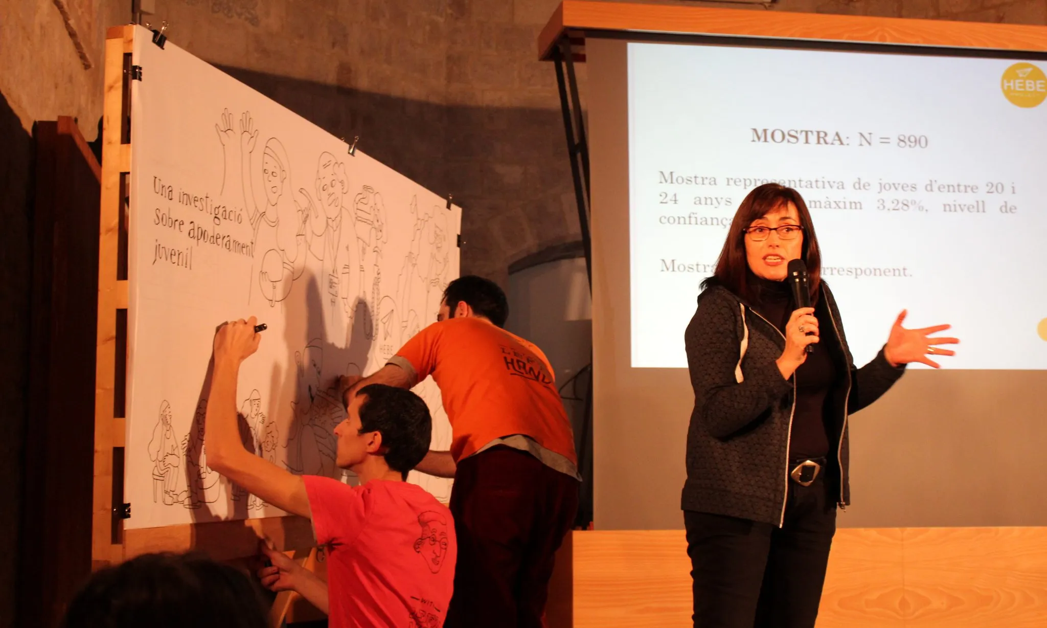 Una dona explicant del Projecte HEBE mentre dos joves il·lustren l'apoderament juvenil en un mural in-situ.