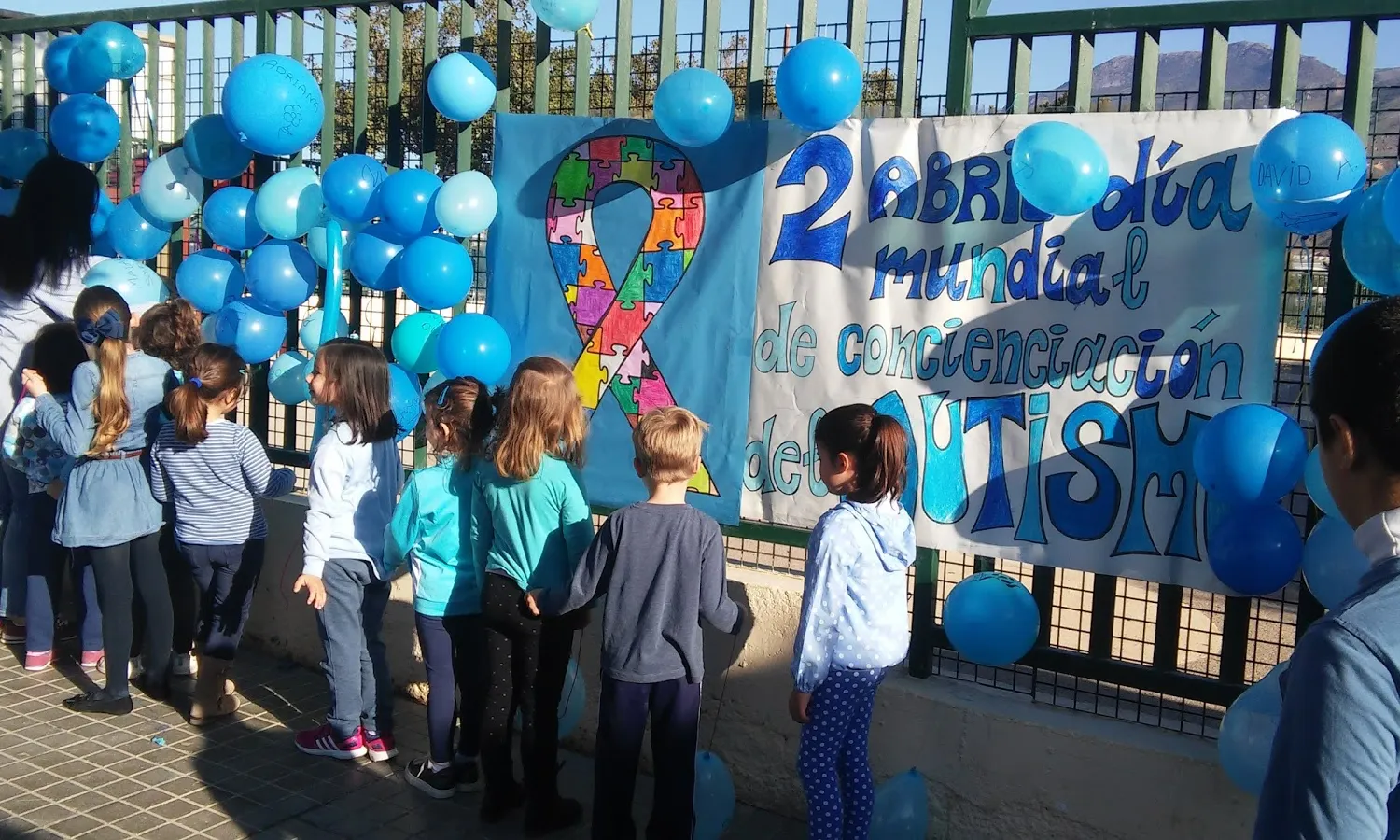 Infants celebrant el Dia mundial de conscienciació sobre l'autisme, amb una pancarta i globus blaus.