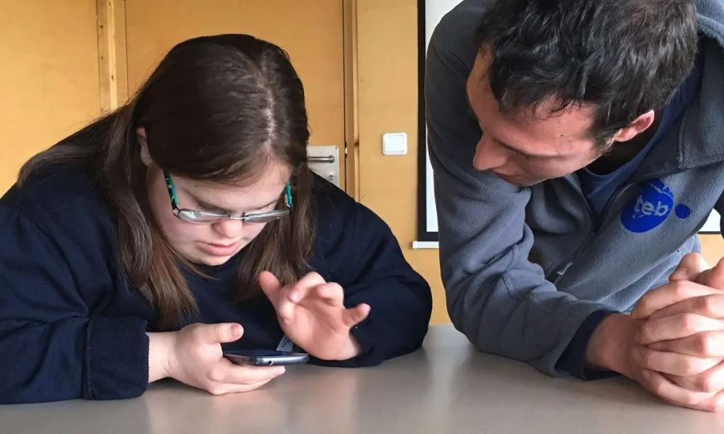 Noia amb síndrome de Down fa servir un telèfon mòbil davant d'un monitor