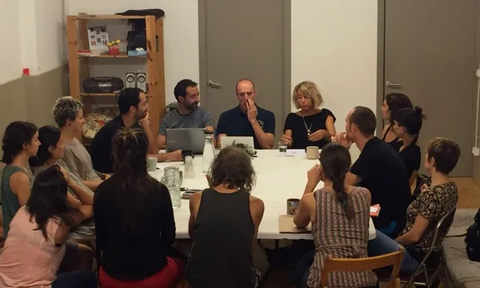 Un grup de persones assegudes al voltant d'una taula duent a terme una sessió amb el grup terapèutic 'El mirall' de la Cooperativa Cos.