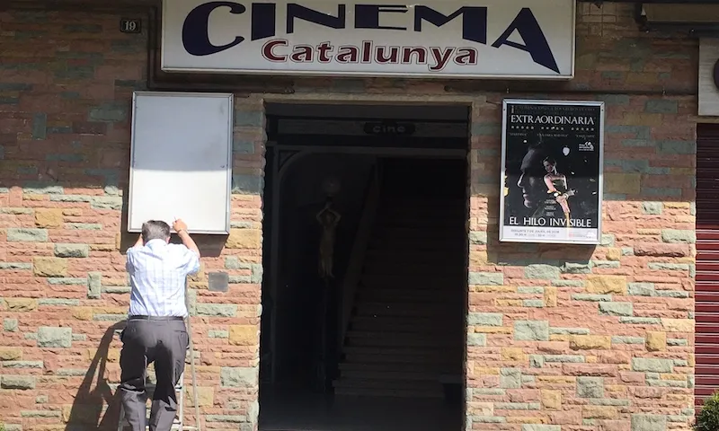 Façana del Cinema Catalunya de Ribes de Freser, amb un home penjant un cartell d'una pel·lícula.