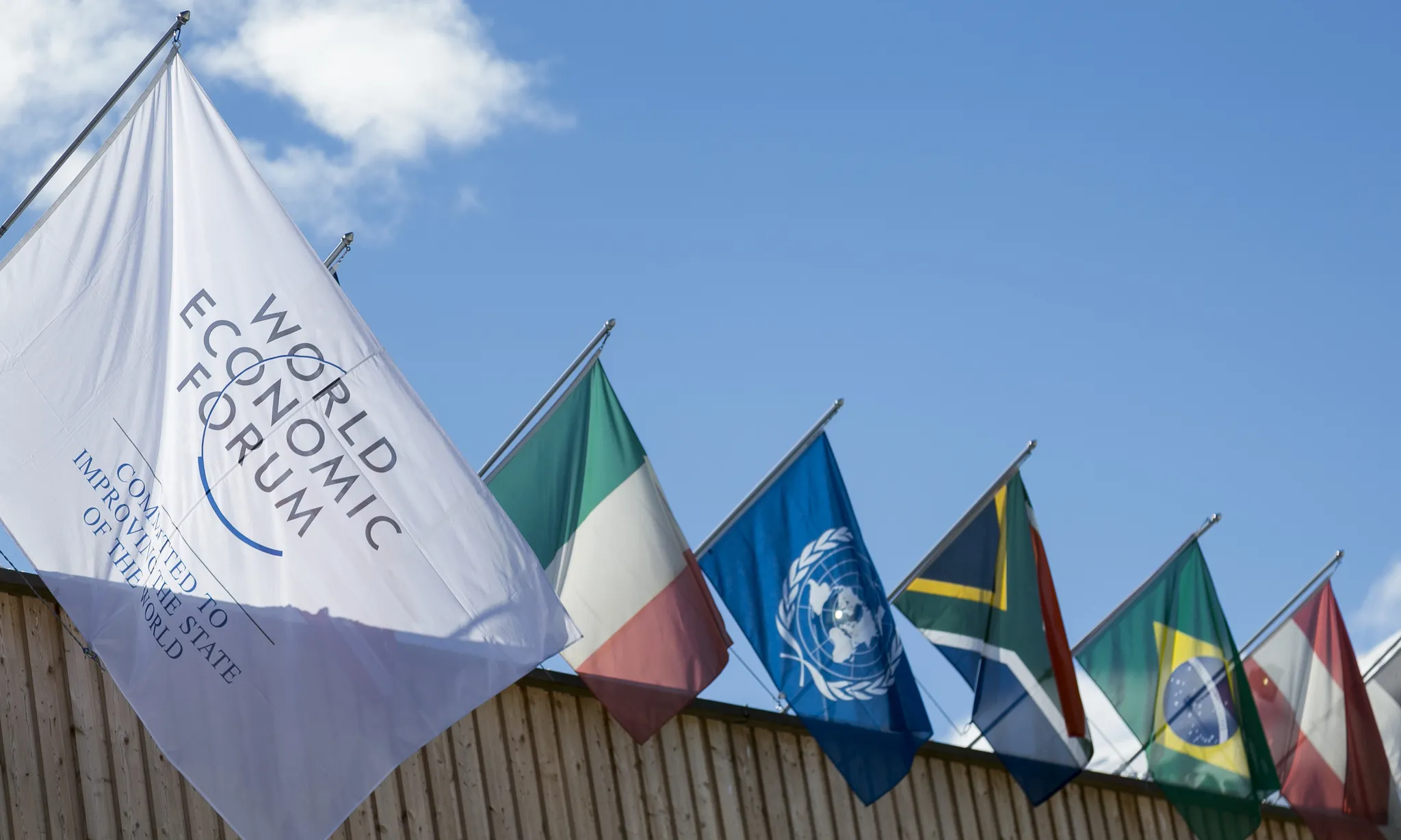 La bandera del Fòrum Econòmic Mundial onejant a l'edifici on se celebra la trobada, juntament amb banderes de diferents països.