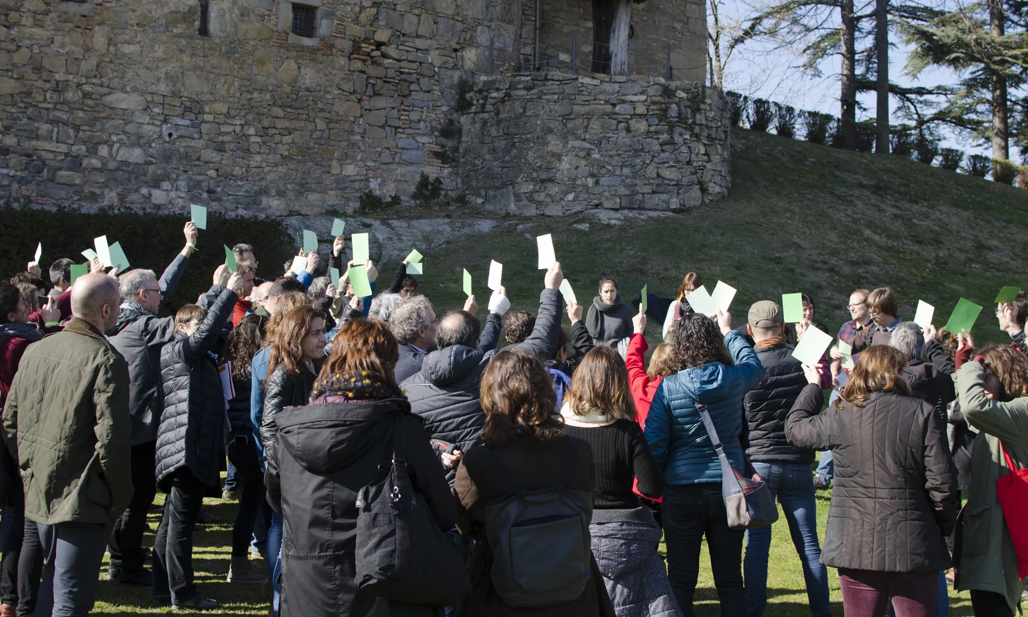 Els membres de les dos xarxes d'entitats, la XCT i la XVAC, estan a fora del Castell de Montesquiu sobre la gespa votant sí al projecte de fusió, amb cartolines verdes.