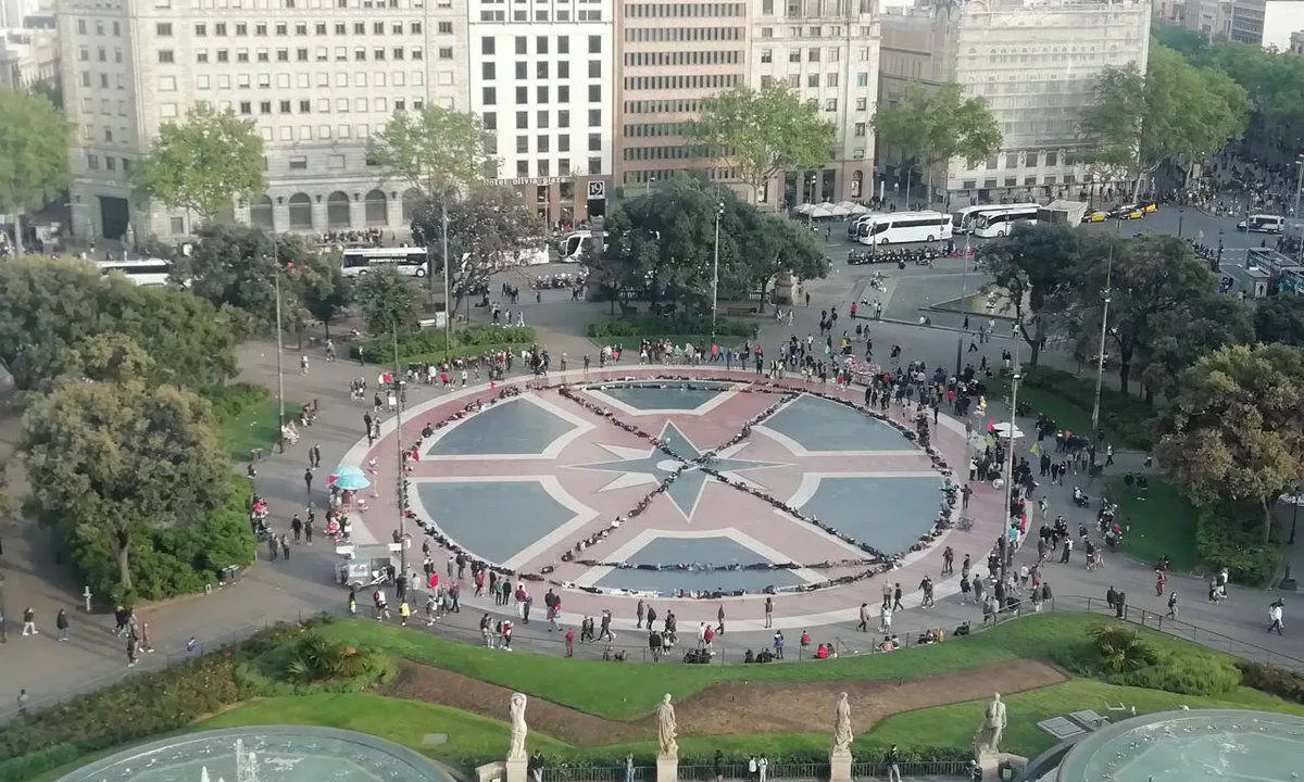200 persones estirades al terra de la plaça catalunya de Barcelona, formant un cercle amb un rellotge de sorra a dins.