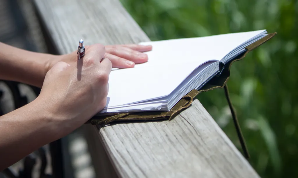 Persona amb llibreta en blanc i bolígraf en mà a punt per escriure