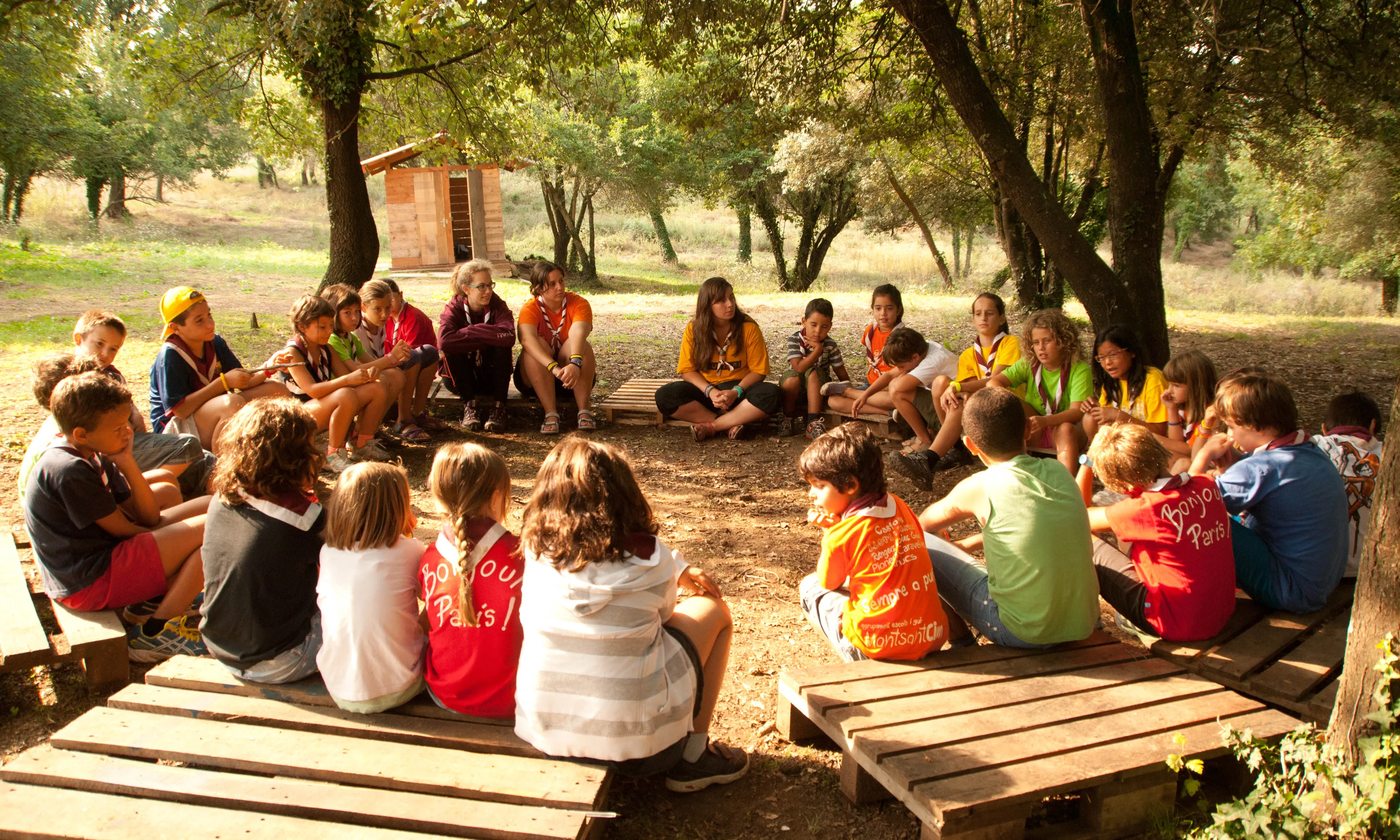 Un grup d'infants asseguts en rotllana damunt d'uns palés.
