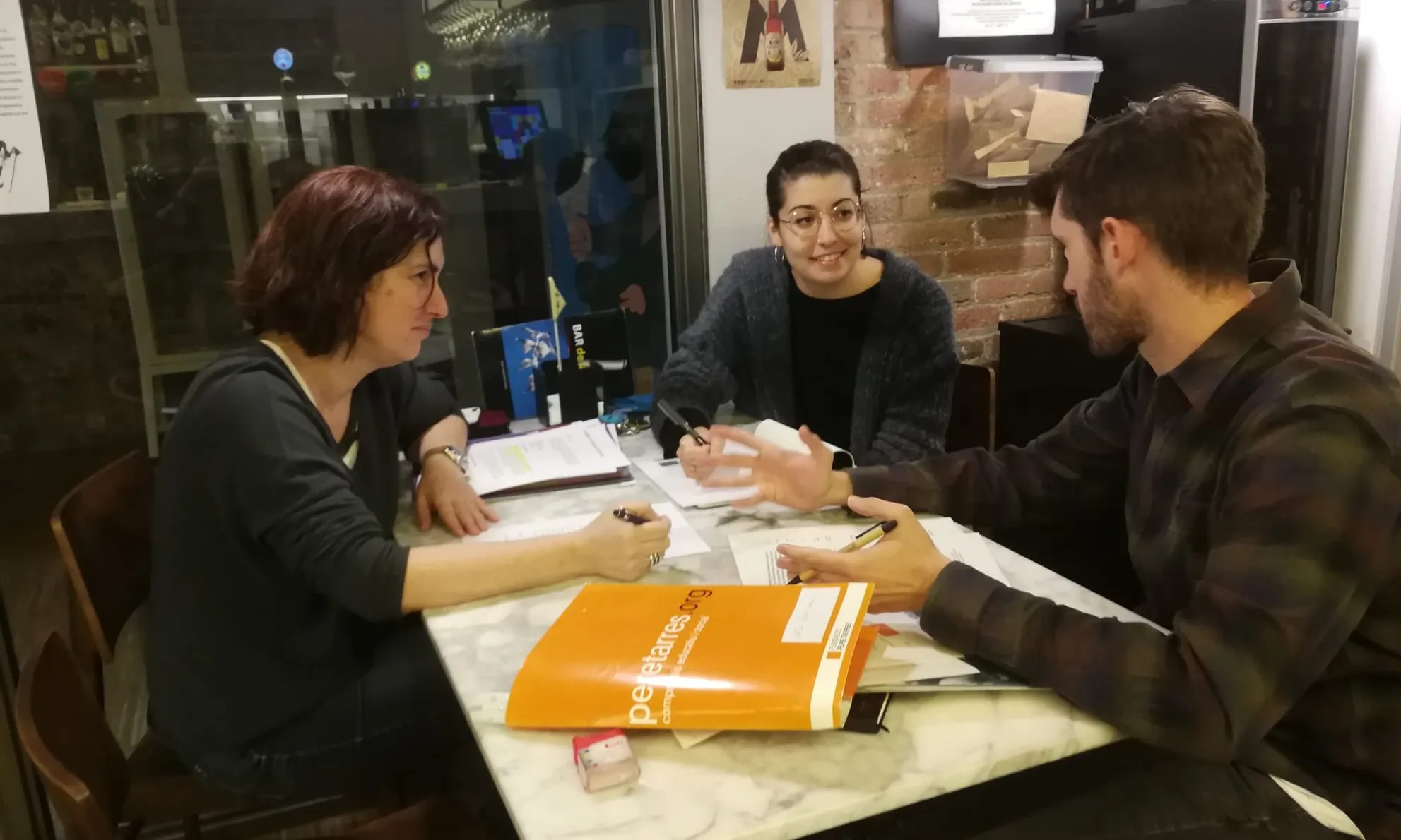 2 noies i un noi al voltant d'una taula en una sessió del servei d'acompanyament