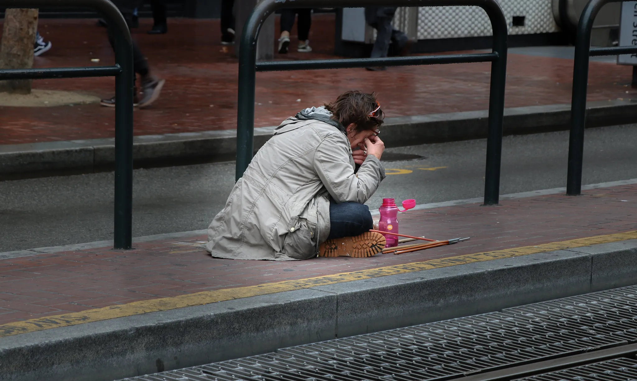 Noia asseguda a terra tapant-se la cara en una estació de tren