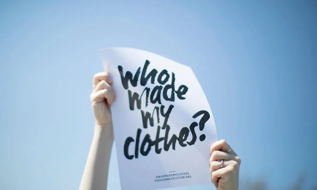 Mans aixecant un cartell que diu 'Who made my clothes'