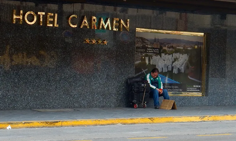 Fotografia d'una persona demanant caritat davant un hotel de luxe. Imatge de Brett Hodnett. Llicència d'ús CC BY-SA 2.0