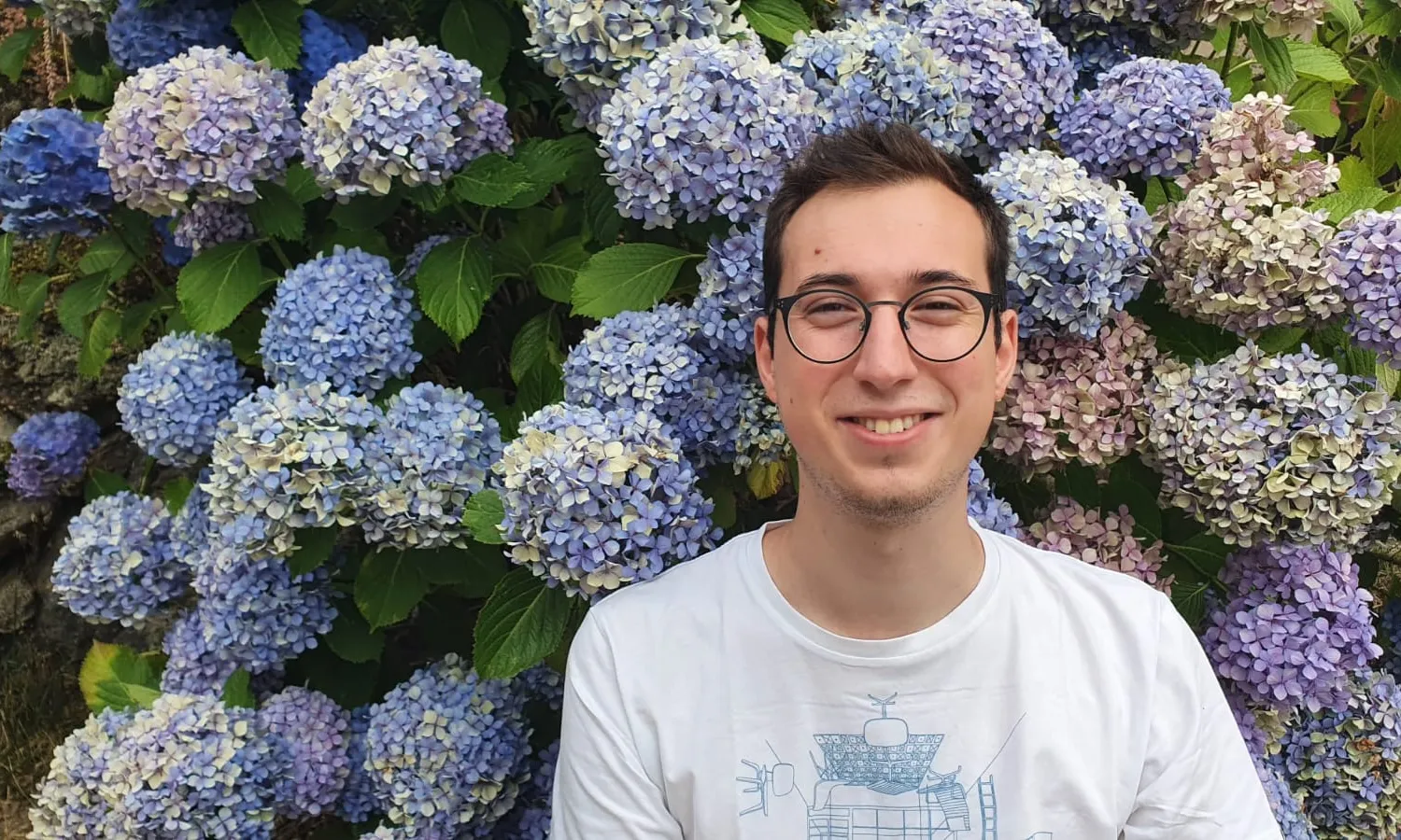 Primer pla d'un noi somrient i flors de fons