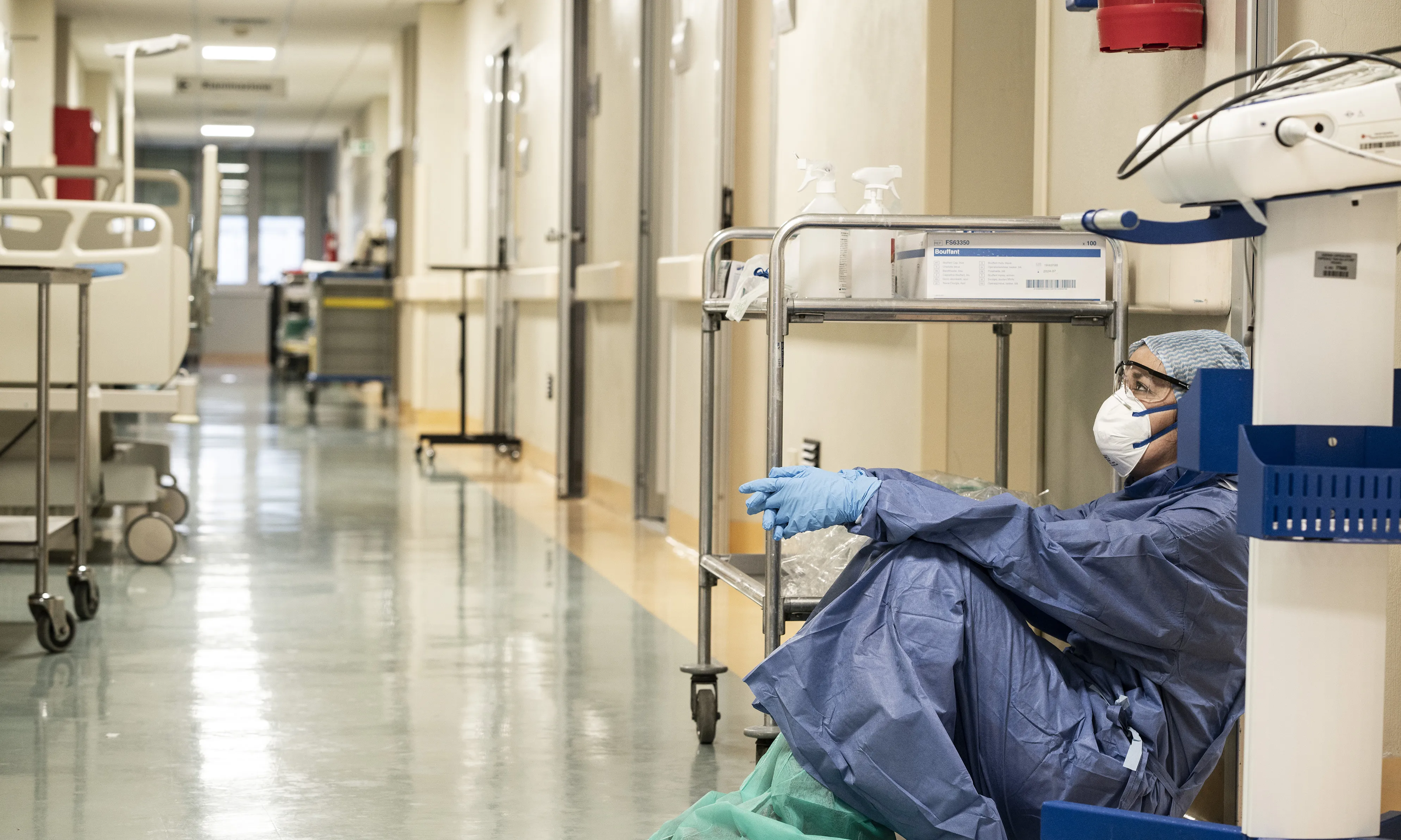 Una infermera amb un EPI jau al terra en un hospital.